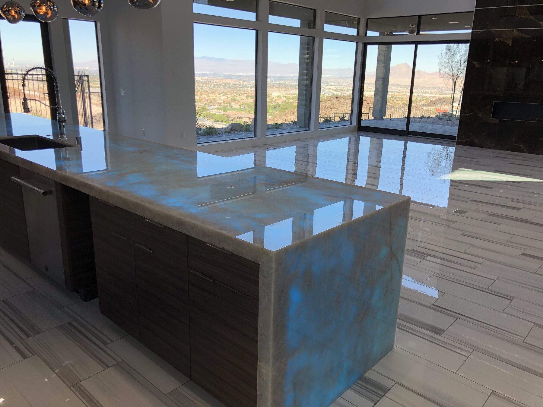 Detail of the backlit onyx countertop in teal, with the valley visible through the windows behind it