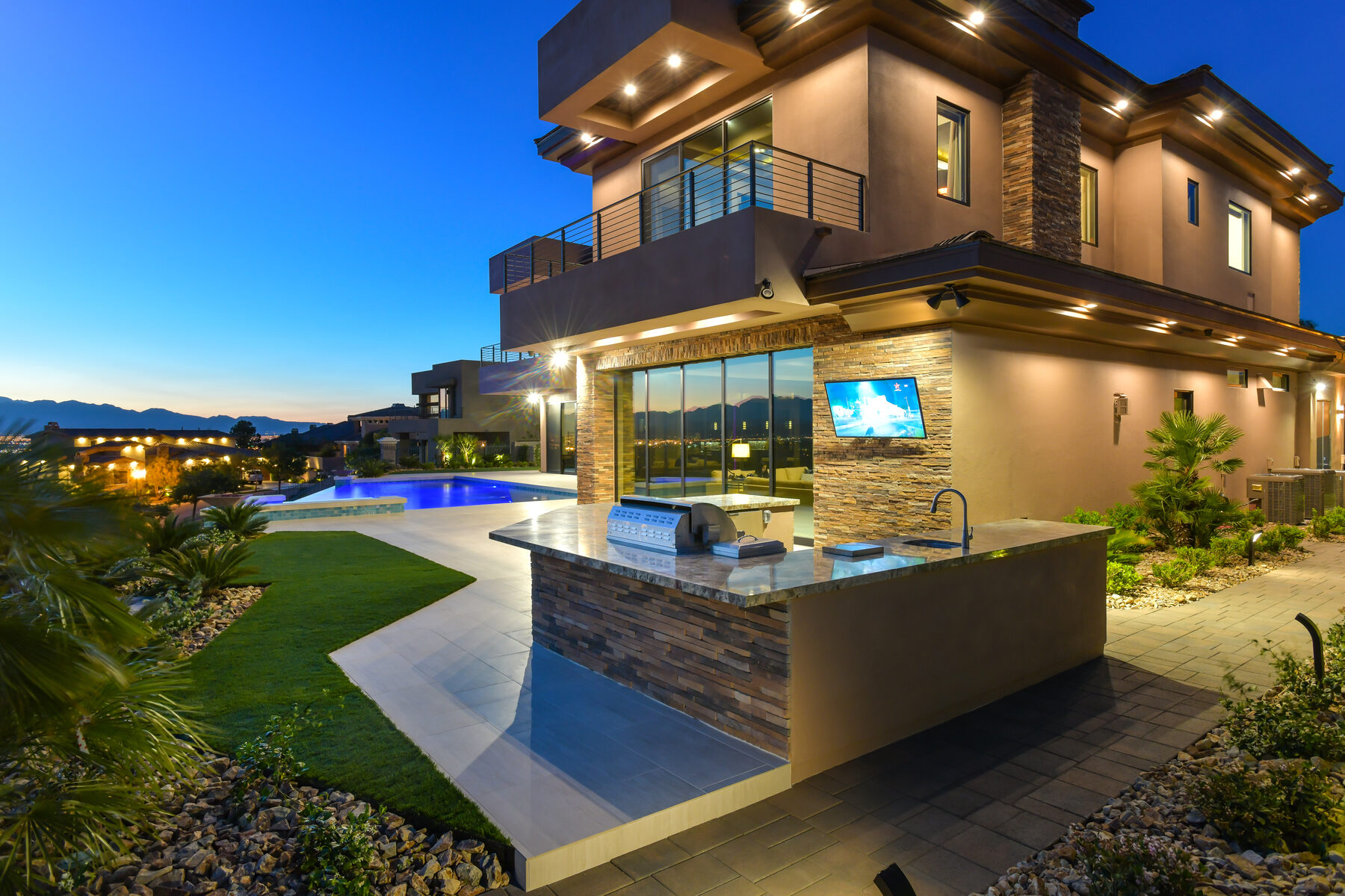The residence at dusk with the outdoor kitchen, pool and exterior accent lighting all lit