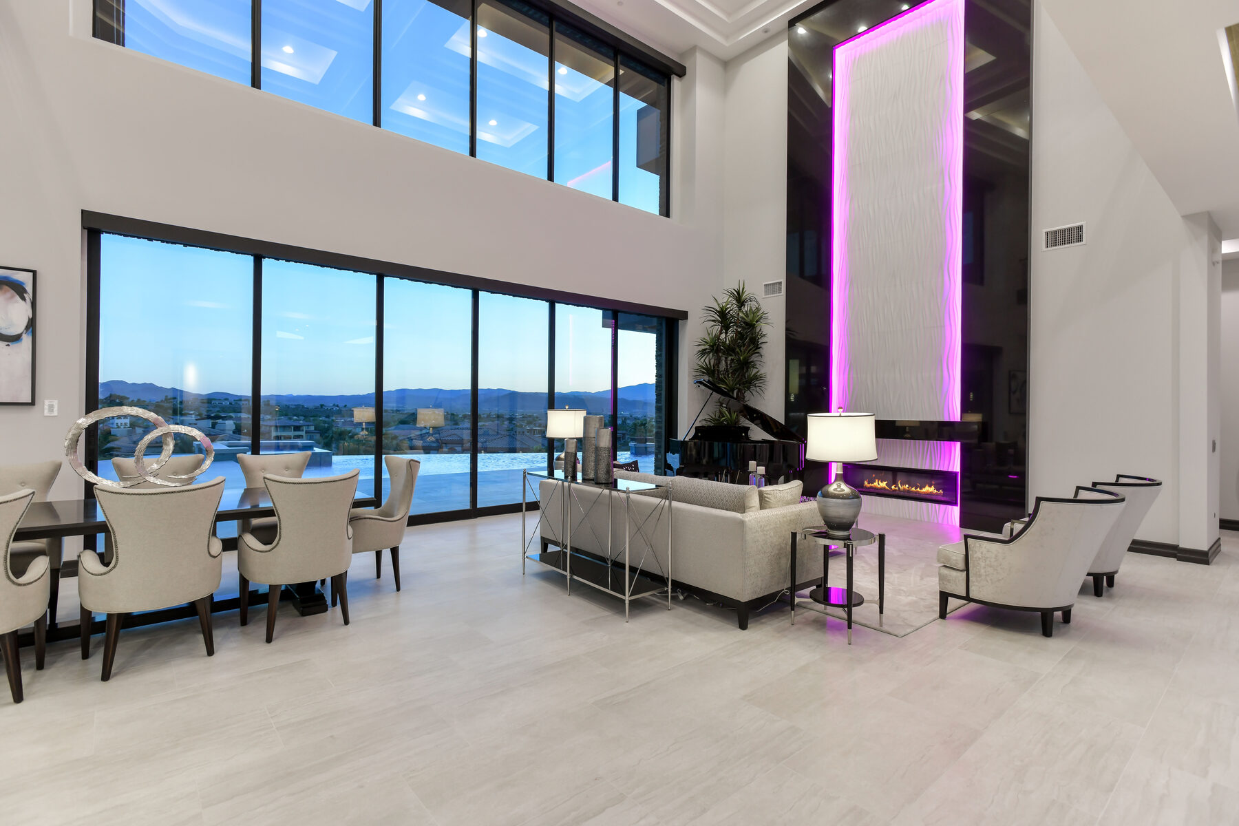 Double height great room with a floor to ceiling fireplace column washed in magenta RGB accent lighting, mountains beyond the window wall