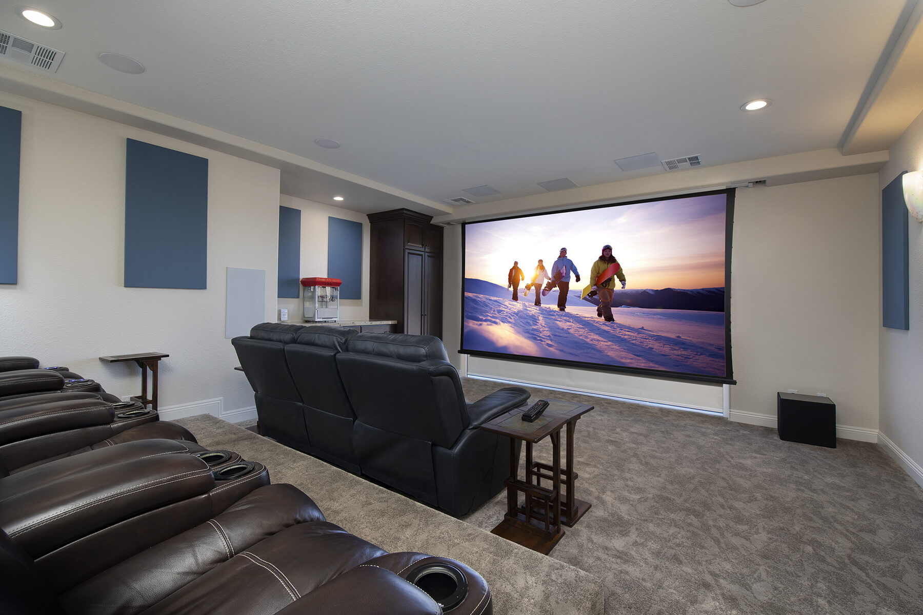 The theater with the 164 inch fixed-frame screen down and tiered recliner seating, acoustic panels on the side walls