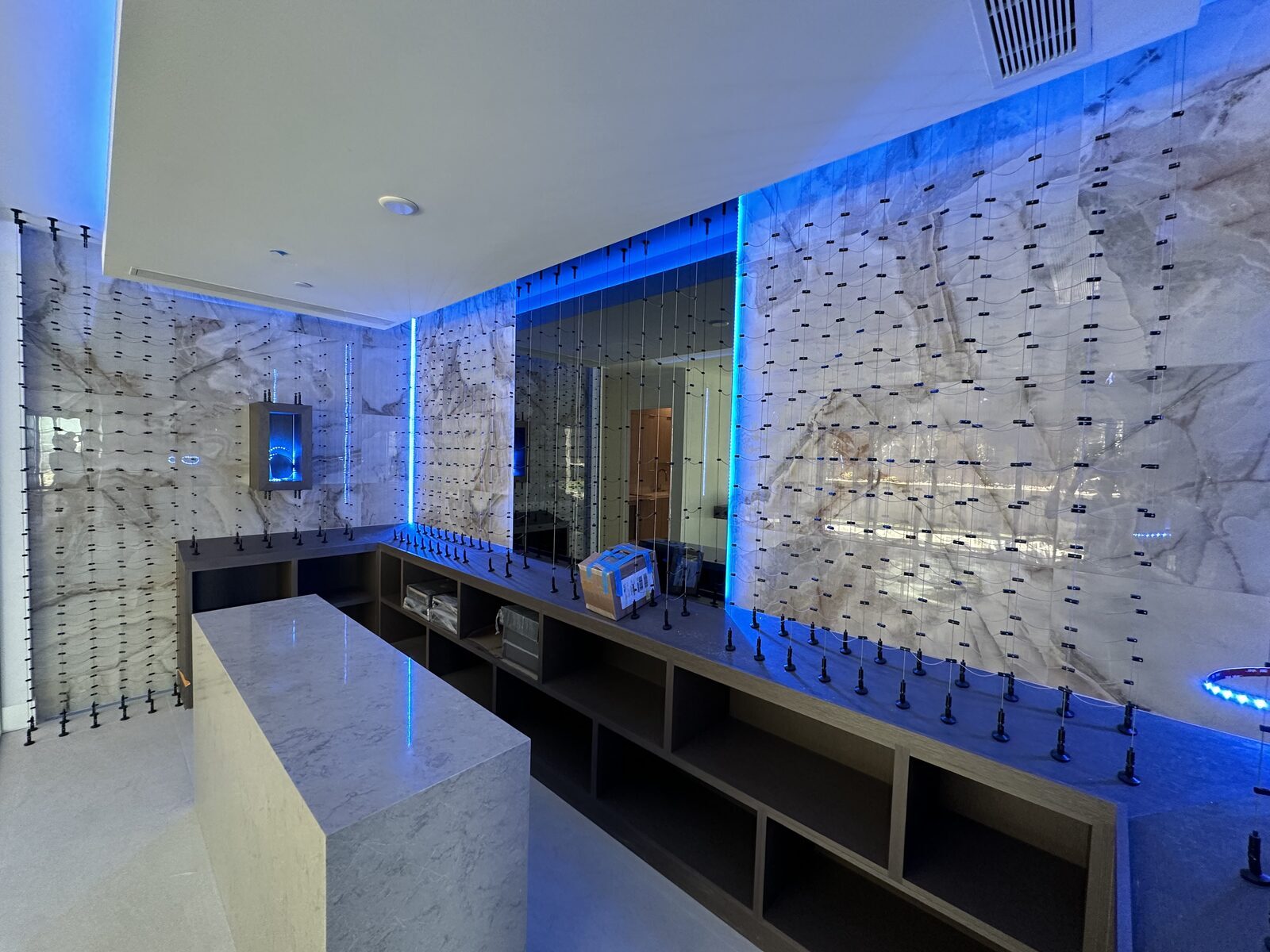 Wine display wall backlit in blue behind marble, with cabinetry and a stone island in front