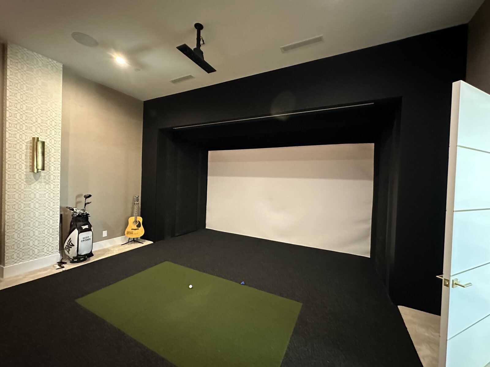 Golf simulator room with a floor to ceiling impact screen, ceiling mounted projector and a putting surface