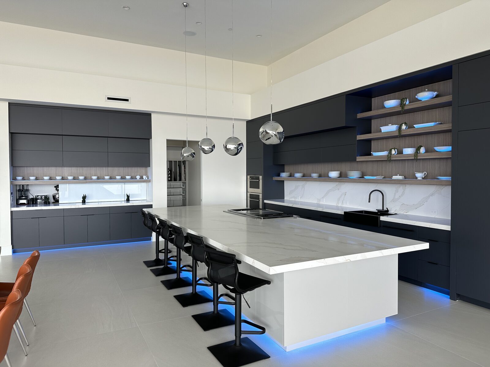 Kitchen island lit from beneath with concealed accent lighting, marble waterfall counter and open shelving beyond