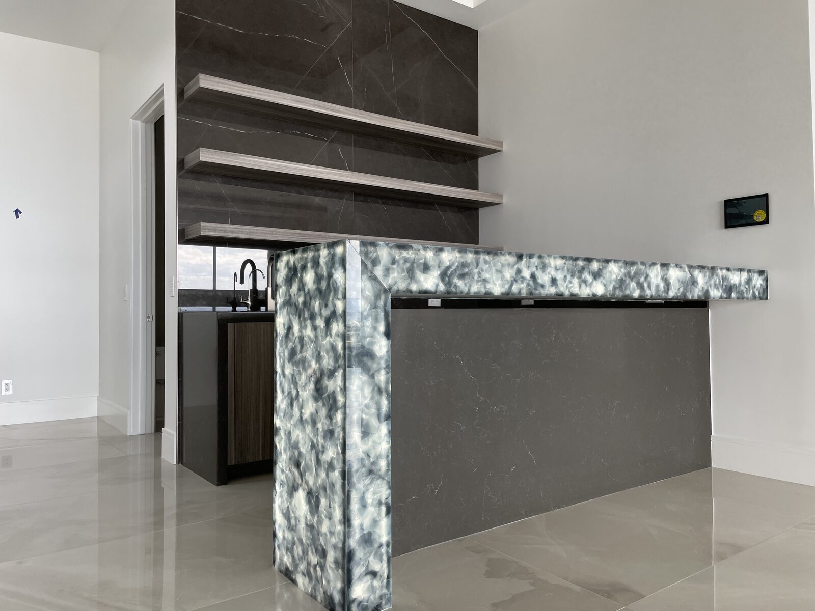 Bar with a blue and white marble waterfall counter and floating stone shelves behind