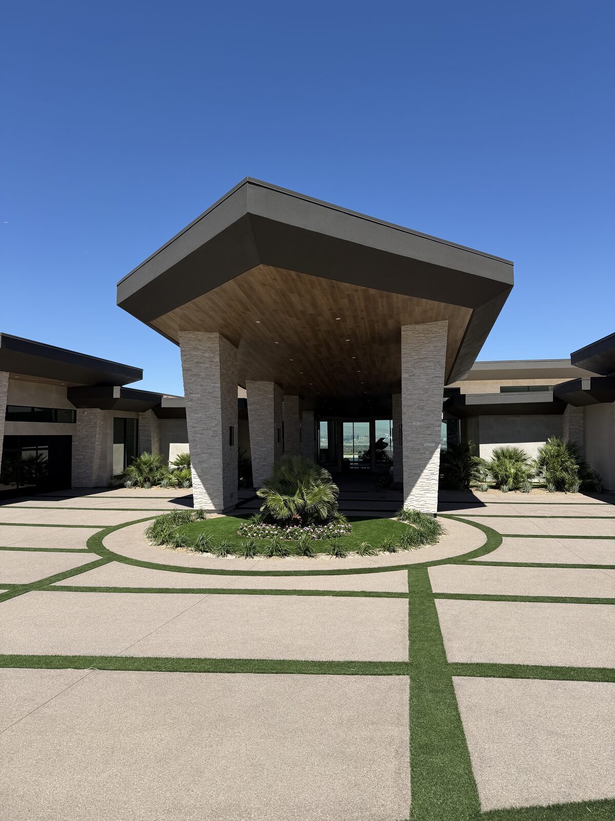 Contemporary porte-cochère entry with a cantilevered wood soffit and stone piers over a circular drive