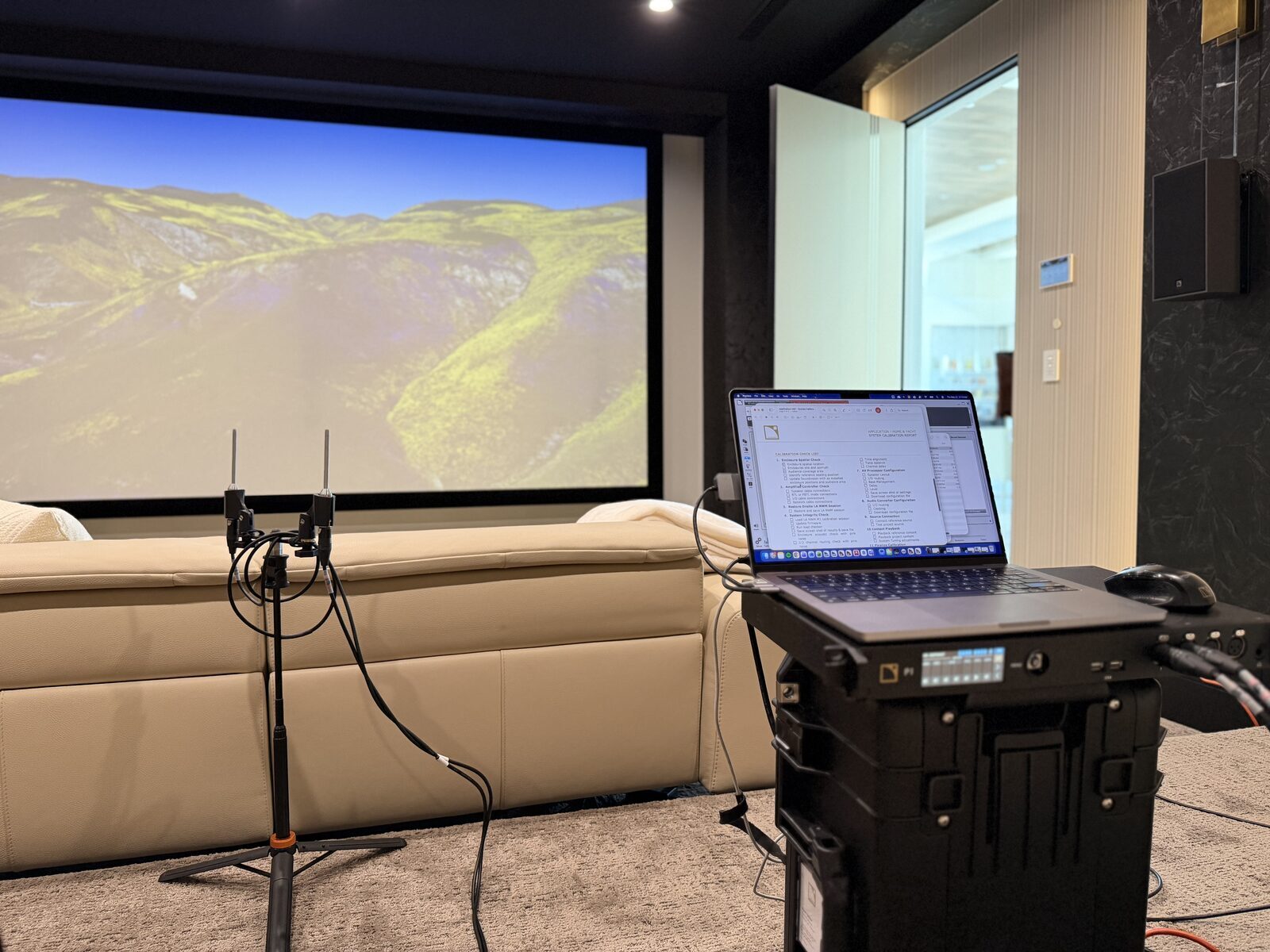 Theater during calibration, with a pair of measurement microphones on a stand in front of the screen and the measurement rig set up behind the seating